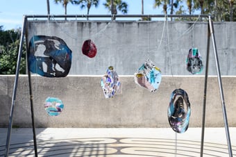 a swing set outside, instead of seats, the thin silver chains are connected to blown glass that hangs at varying lengths