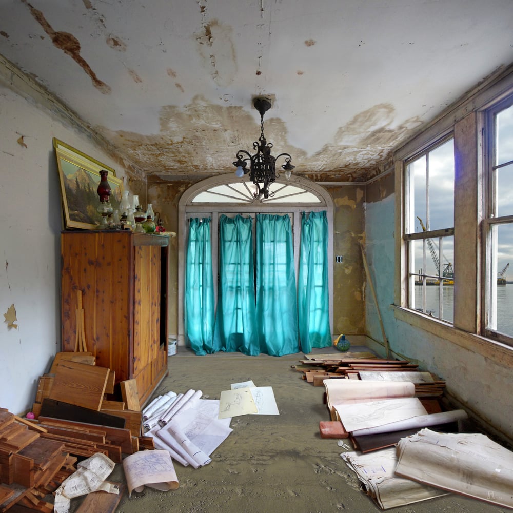 a water damaged room with a floor made of sand. piles of blueprints lay on the right hand side under a set of windows over looking water with cranes. on the left hand side is a wardrobe made of wood with more blueprints and pieces of wood. At the very end of the room is a set of French Doors with blue curtains. 