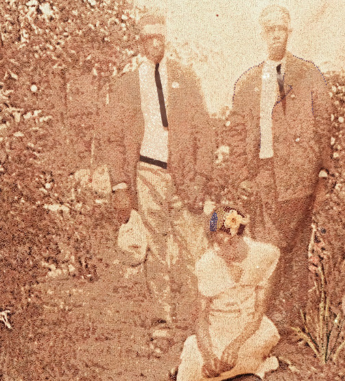 in a sepia colored screenprint, two Black men stand next to each other outdoors, a woman sits between them