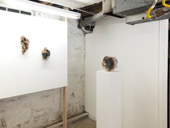 installation view of two sculptures on white wall and one on white pedastal