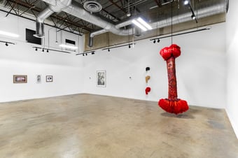 gallery view three white walls large red sculpture in right foreground with four framed artworks hung to the left