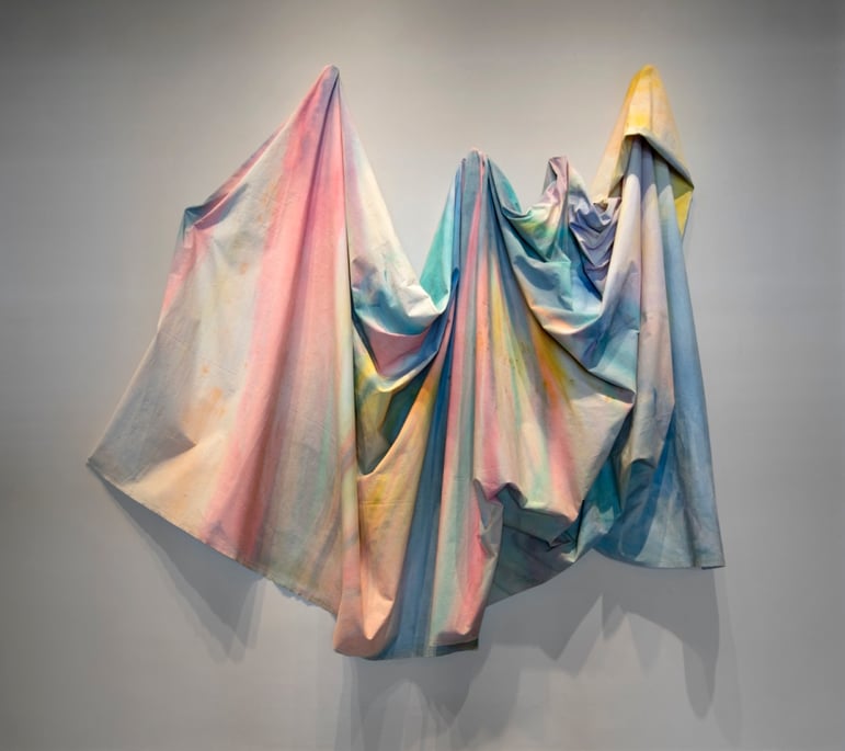 A painting folding, falling off of the wall like drapes. Colors are a light wash of the rainbow. 