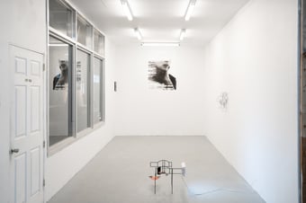 a white walled gallery space with minimal art works on the wall and a small sculpture at the center of the room