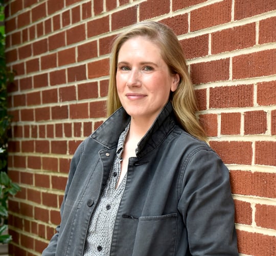 headshot of white, blonde woman leaning against red brick wall
