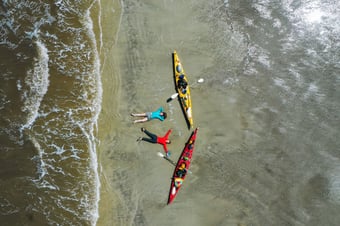 bird's eye view of two people sitting on river shore next to kayaks