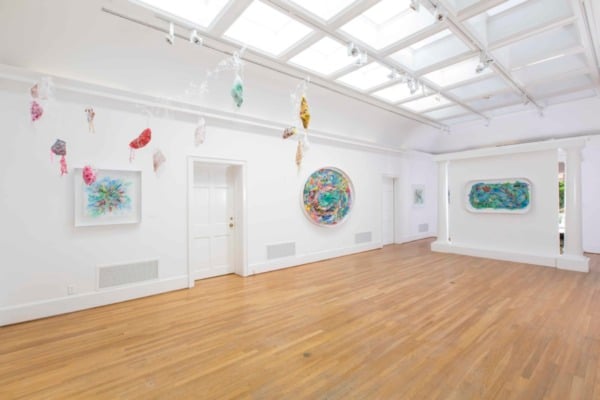 white walled exhibition space with light wooden floors and walls sparsely covered with brightly colored artwork