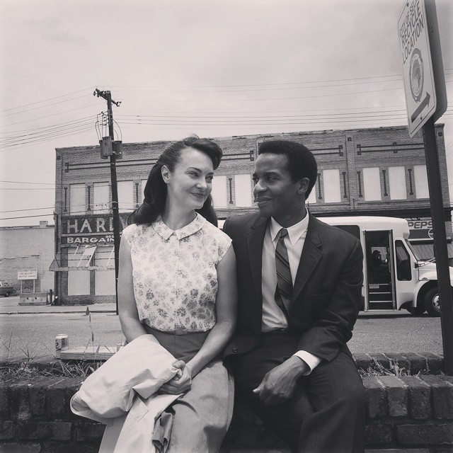artist Tara Ochs in 50's era clothing sitting next to a Black actor