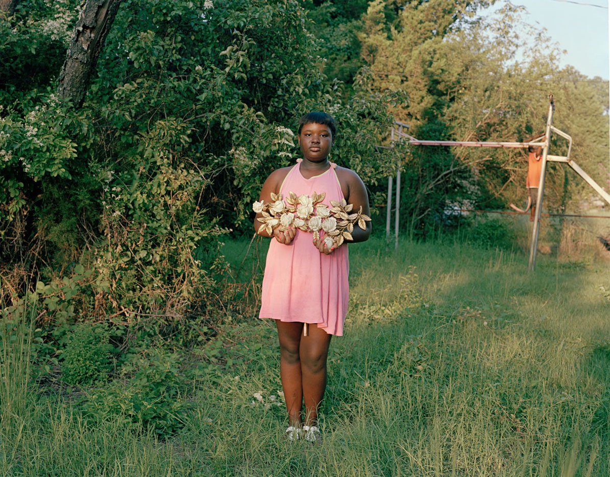 Young woman in a pink dress holds a metal sculpture of white roses in a field. 