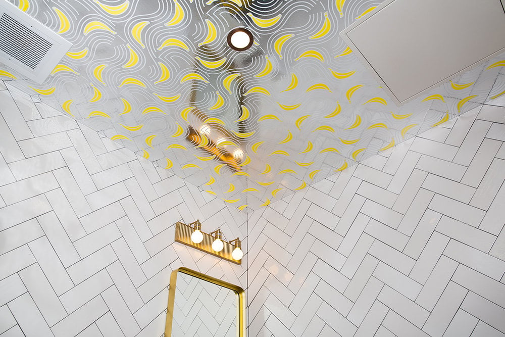 mirrored ceiling of a bathroom with a pattern of curvy lines and small yellow bananas 