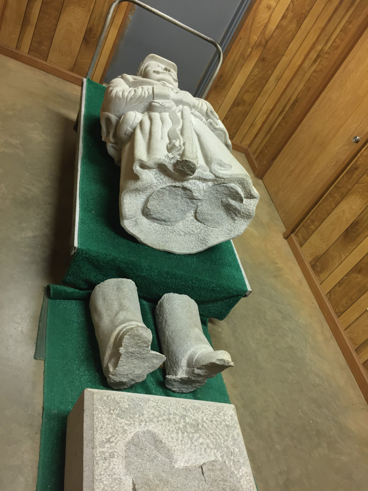 Granite sculpture of a man that is broken into three parts lying on a pedestal. Called Dutchy