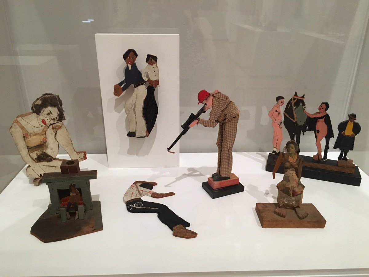 VItrine containing flat, cutout figures, including a white man pointing a rifle at a black man on the ground. 
