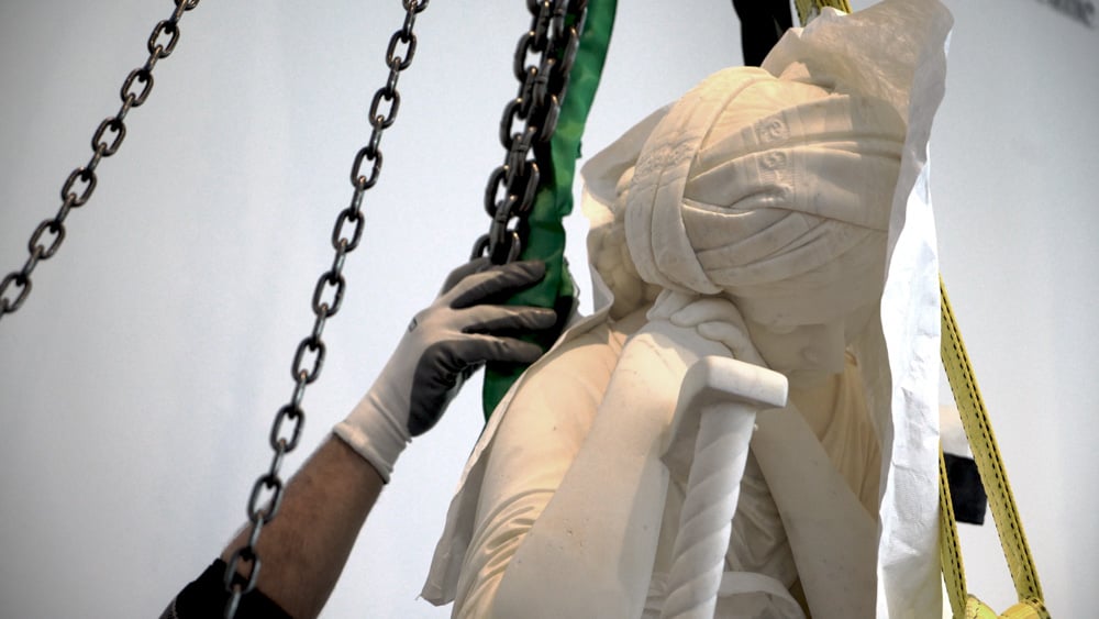 a hand reaching up to make sure chains are secure around marble sculpture 