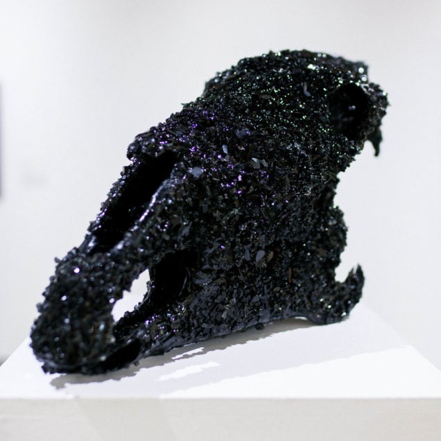 A sculpture by R.C. Hagans of a skull-like shape covered in black tarlike substance and crystals. 