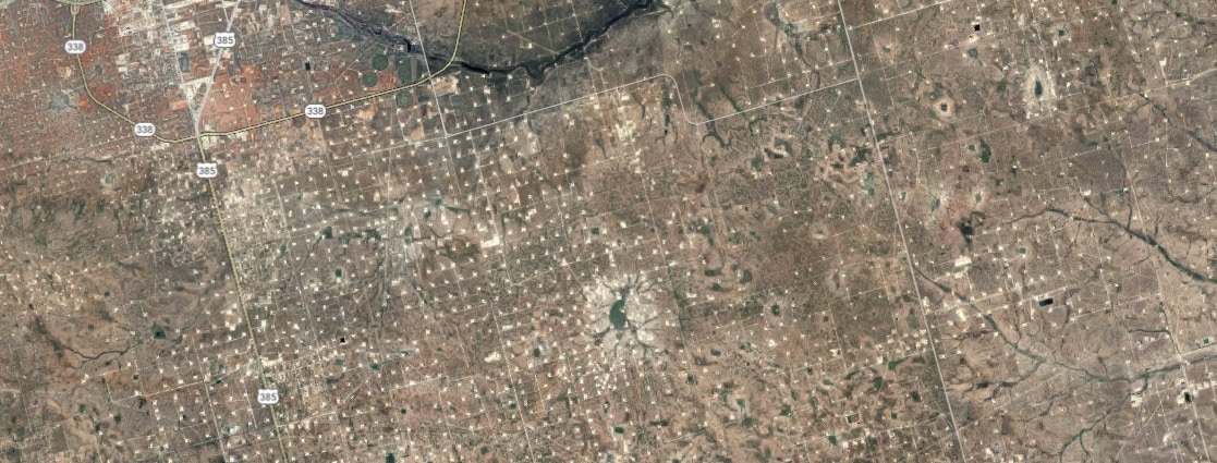 an abstract aerial view of brown earth dotted with white points that are oil wells.
