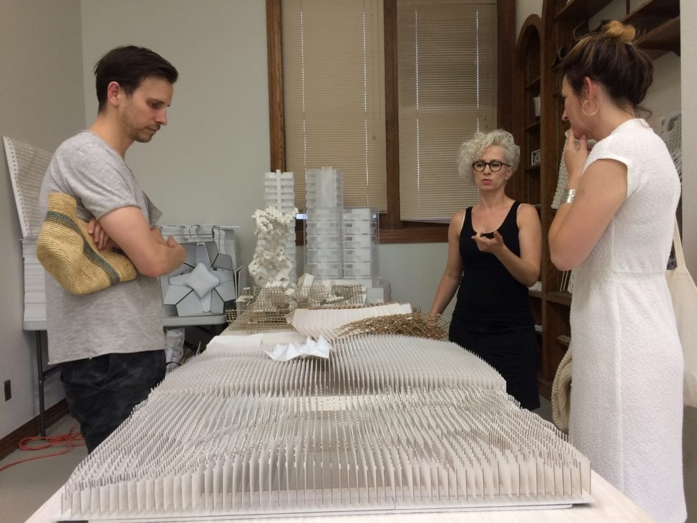 a man and two women standing around a table and discussing the architecture model between them