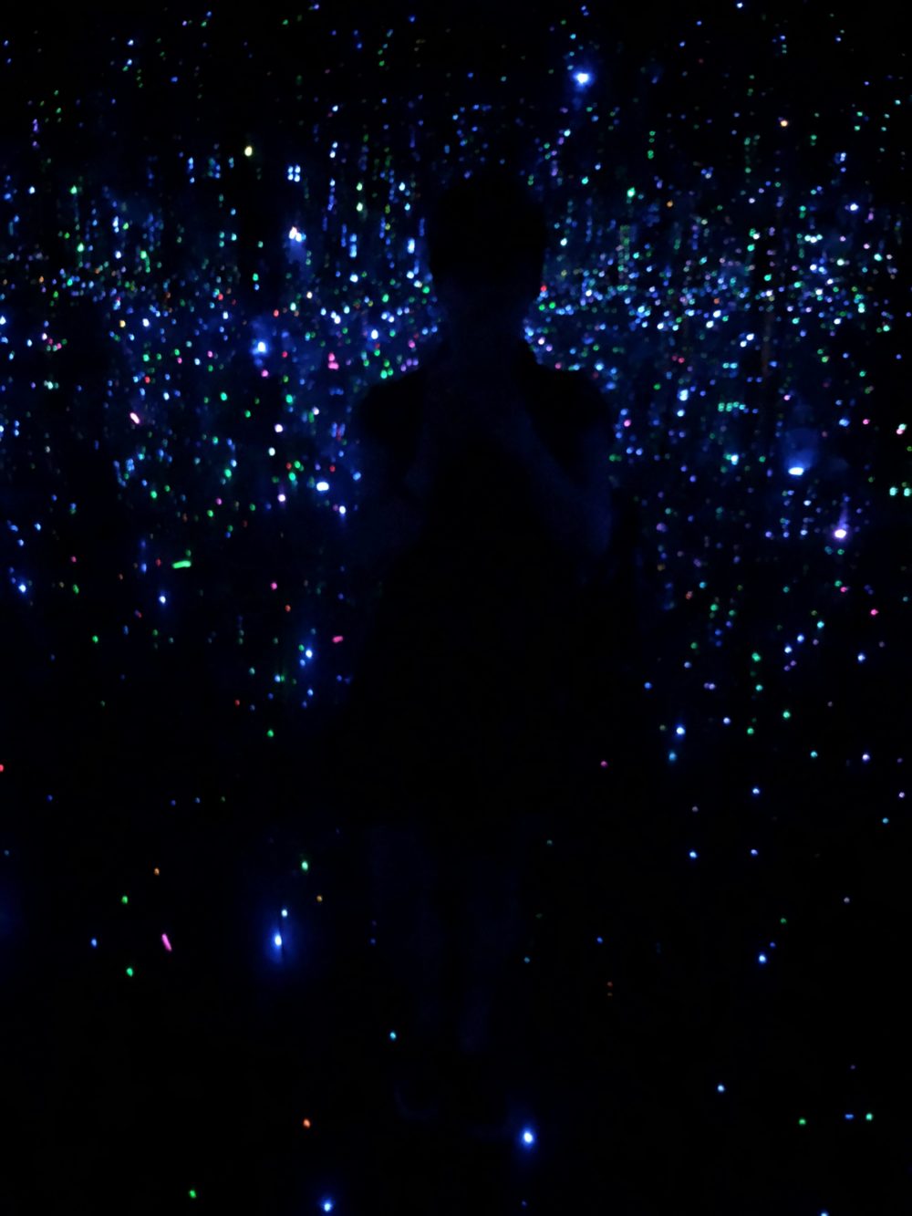 A very dark room with thousands of points of light and a human silhouette.