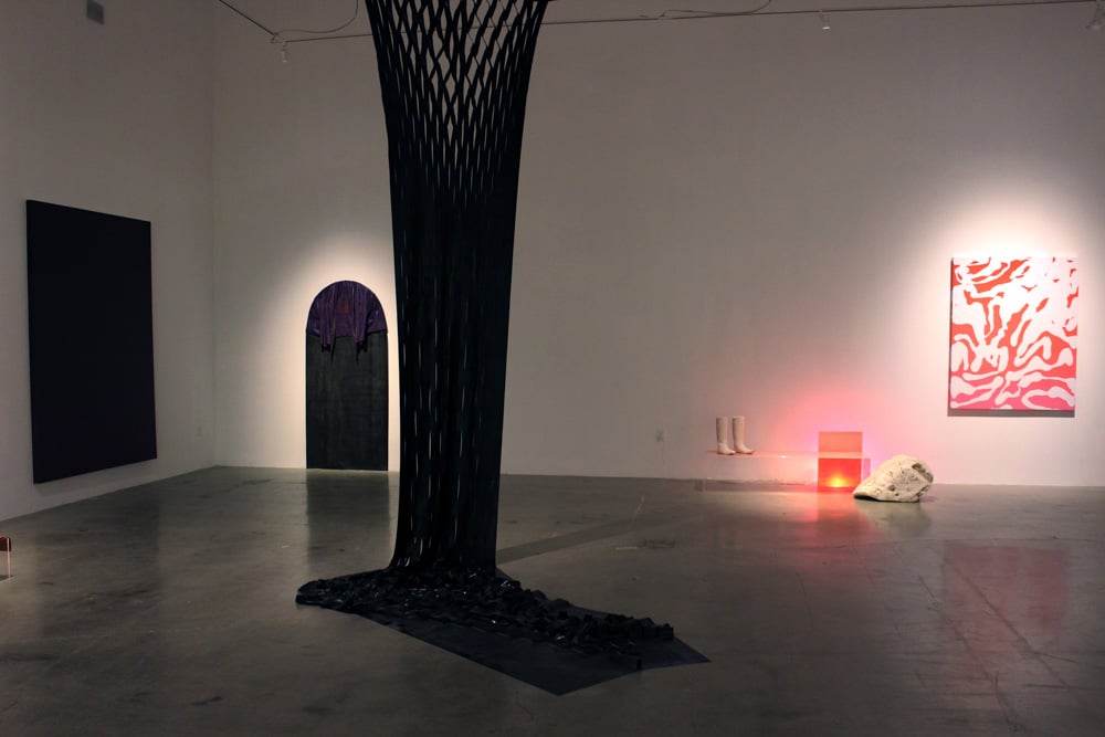 Museum gallery with three wall pieces and a black form suspended in the foreground, by Kirstin MItchell. 