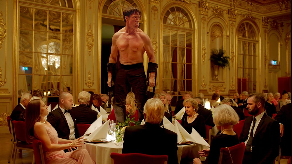 Shirtless performer stands on top of a dinner table at a charity event