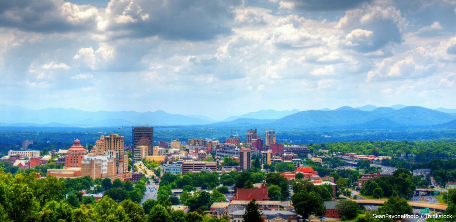 Aerial view of Asheville, with mountains on the horizon and clouds in the sky.