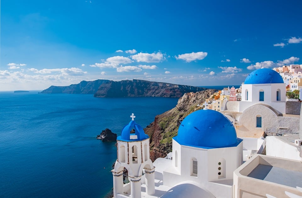 View from high up of blue rooftops on whitewashed buildings with vivid blue sea and sky in the background.