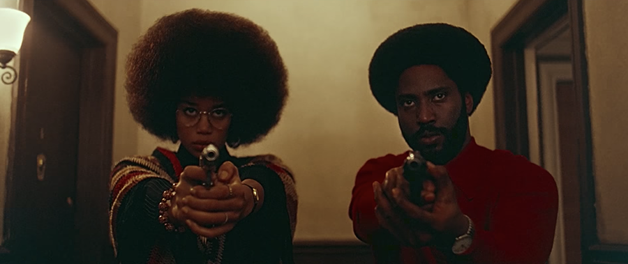 A black man and woman with afros pointing guns at the camera/viewer, in the film Blackkklansman