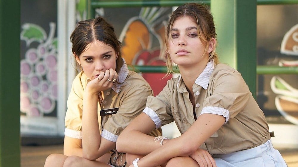 Two young white women in beige waitress uniforms sitting on a curb.