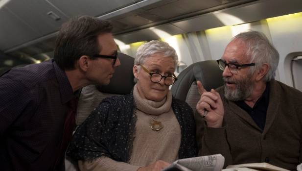 Older woman sitting between two men on a plane who are talking over her.