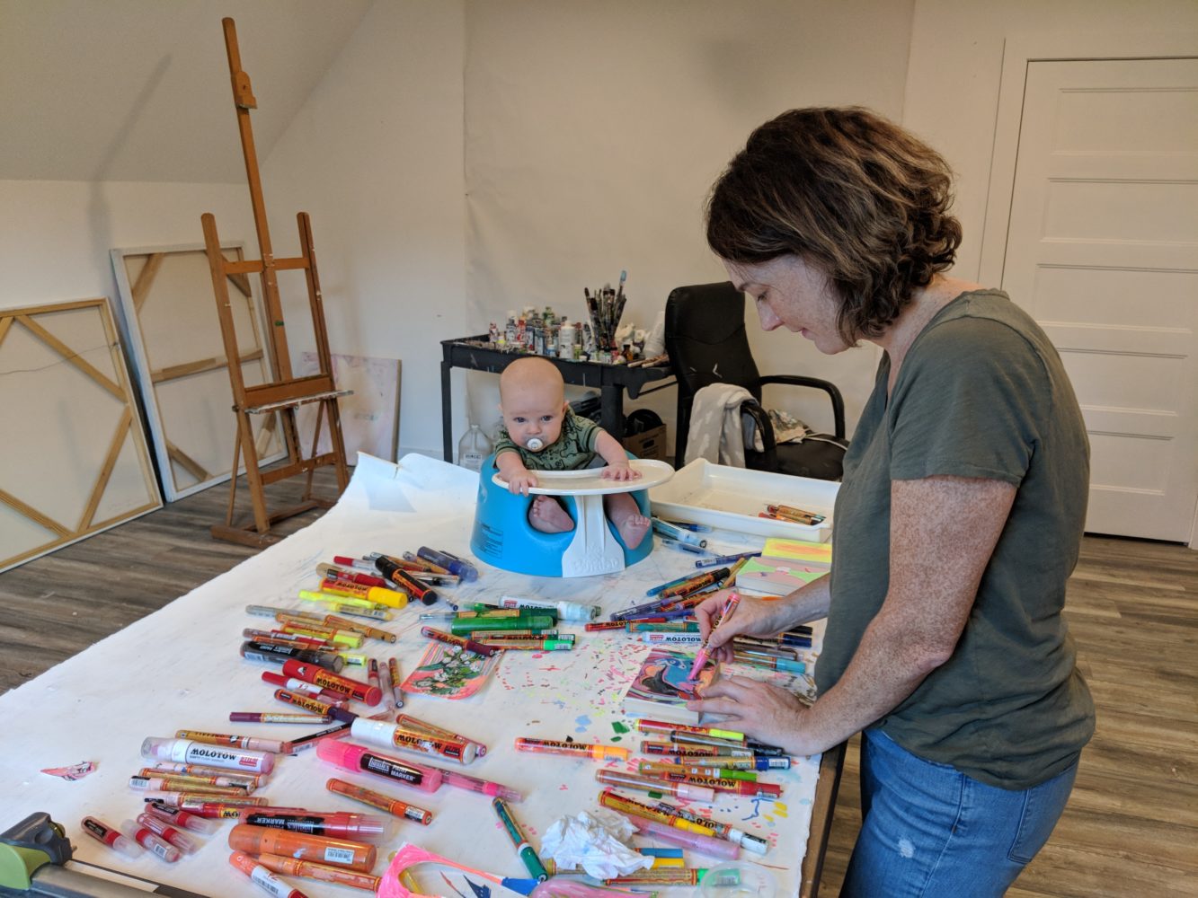 Woman drawing with markers on table with her baby son watching. 