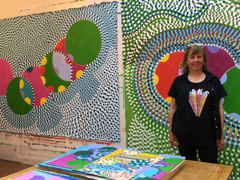 Artist Carol John stands in her studio in front of large geometric paintings