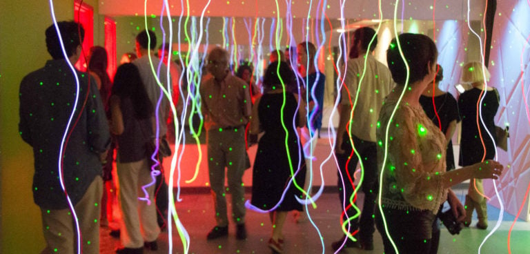 A gropud of people interact under neon lights and strings