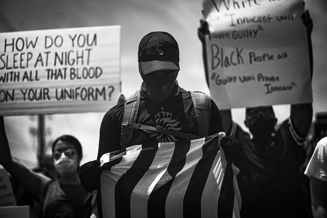 black and white photograph of a man holding an American flag, marching against police brutality 