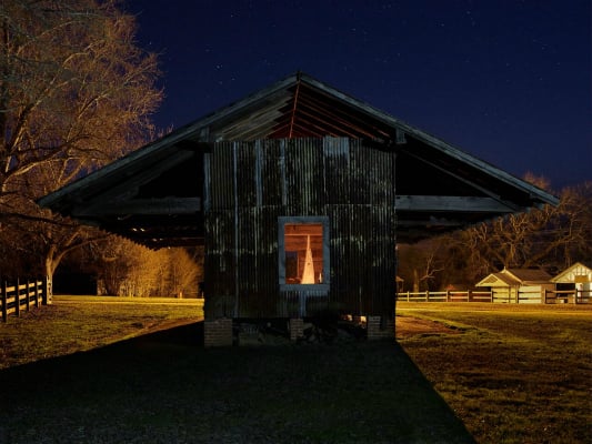 Image of a glowing window on a weathered barn photographed at night. 