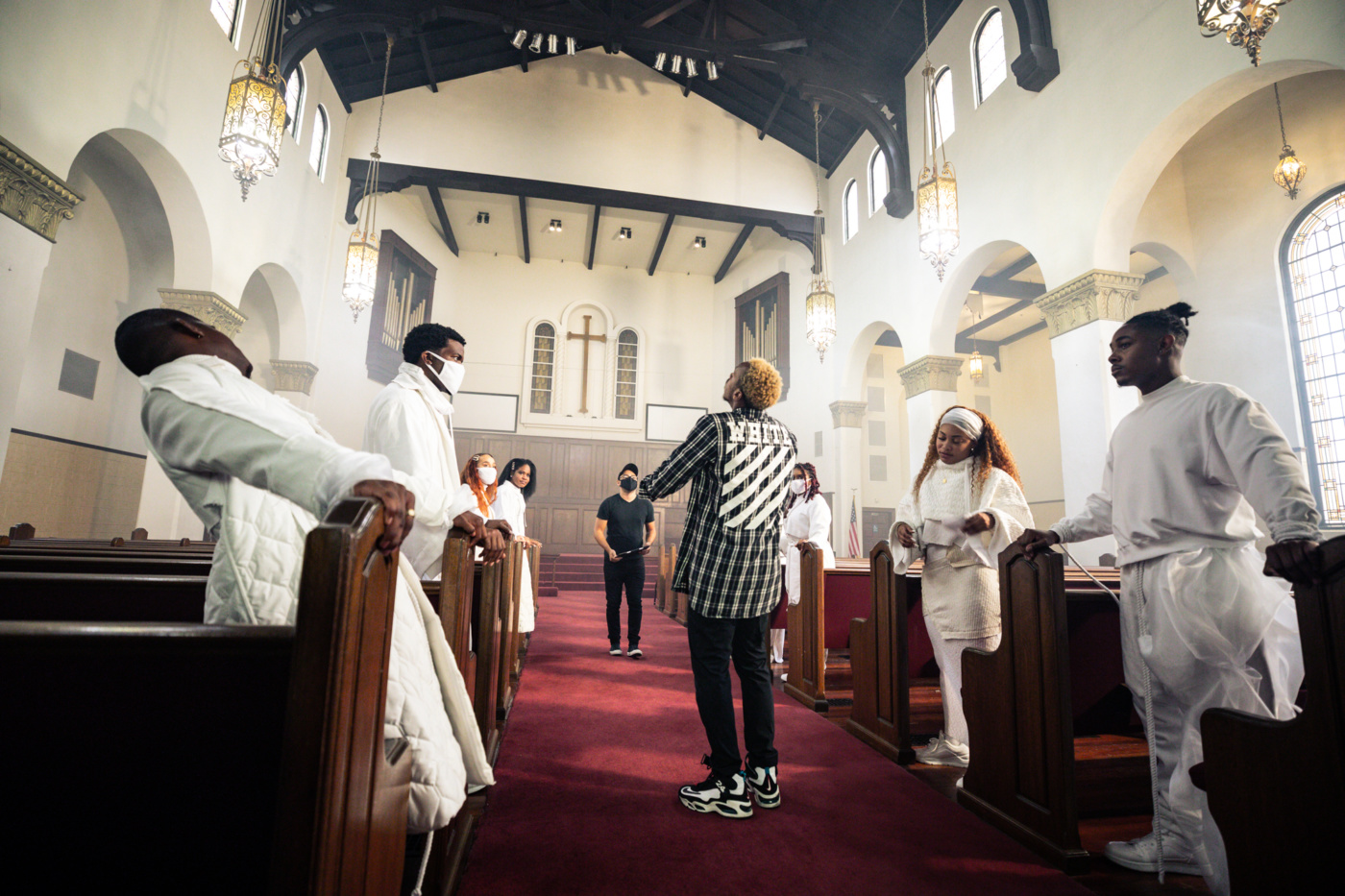 Lil Buck stands surrounded by church choir members dressed all in white between church pews.