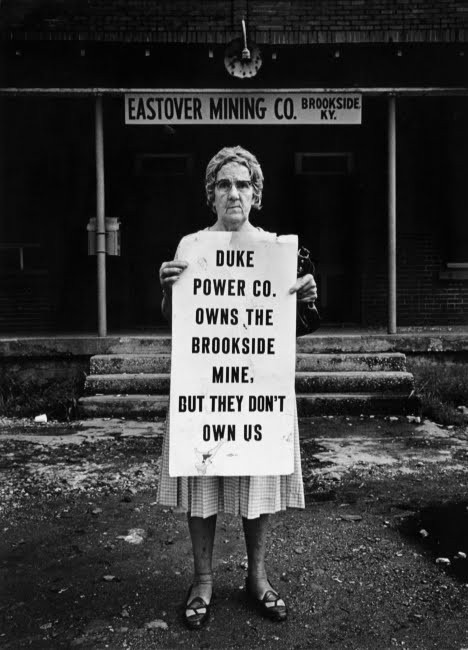 Woman holds a sign that reads "Duke Power Co owns the Brookside Mine, but they don't own us."