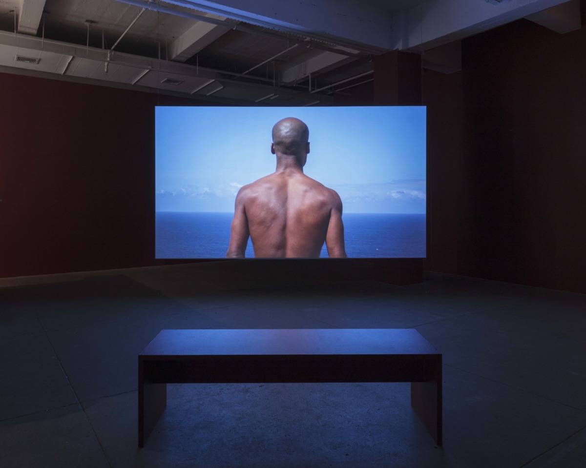 Projection of a video work with the image of a mans bare back, in front of the sea. 