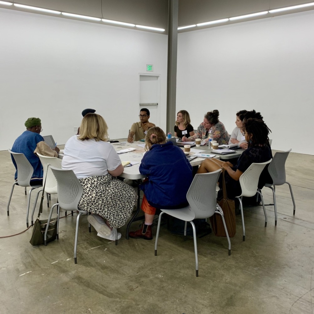a diverse group of students sit around a conference table with laptops and notebooks