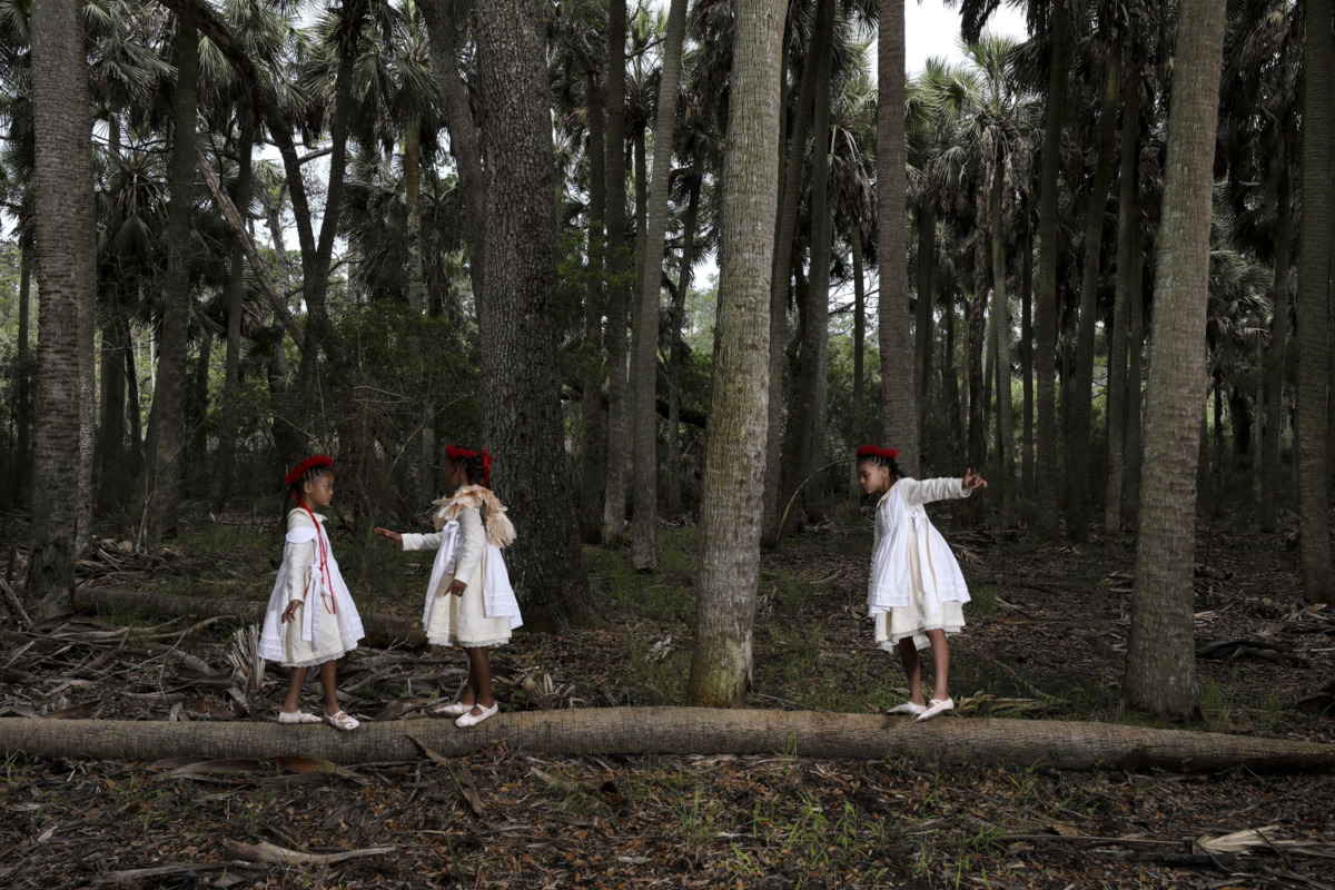 Girls in old fashion white dresses walk along a fallen log in a coastal forrest