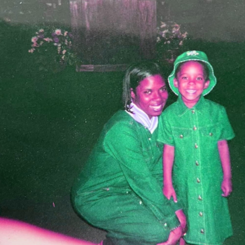 a photo of a mother kneeling next to a small child with a huge grin on their face. the color of the image has been altered so that their skin is hot pink and their clothes a vibrant green