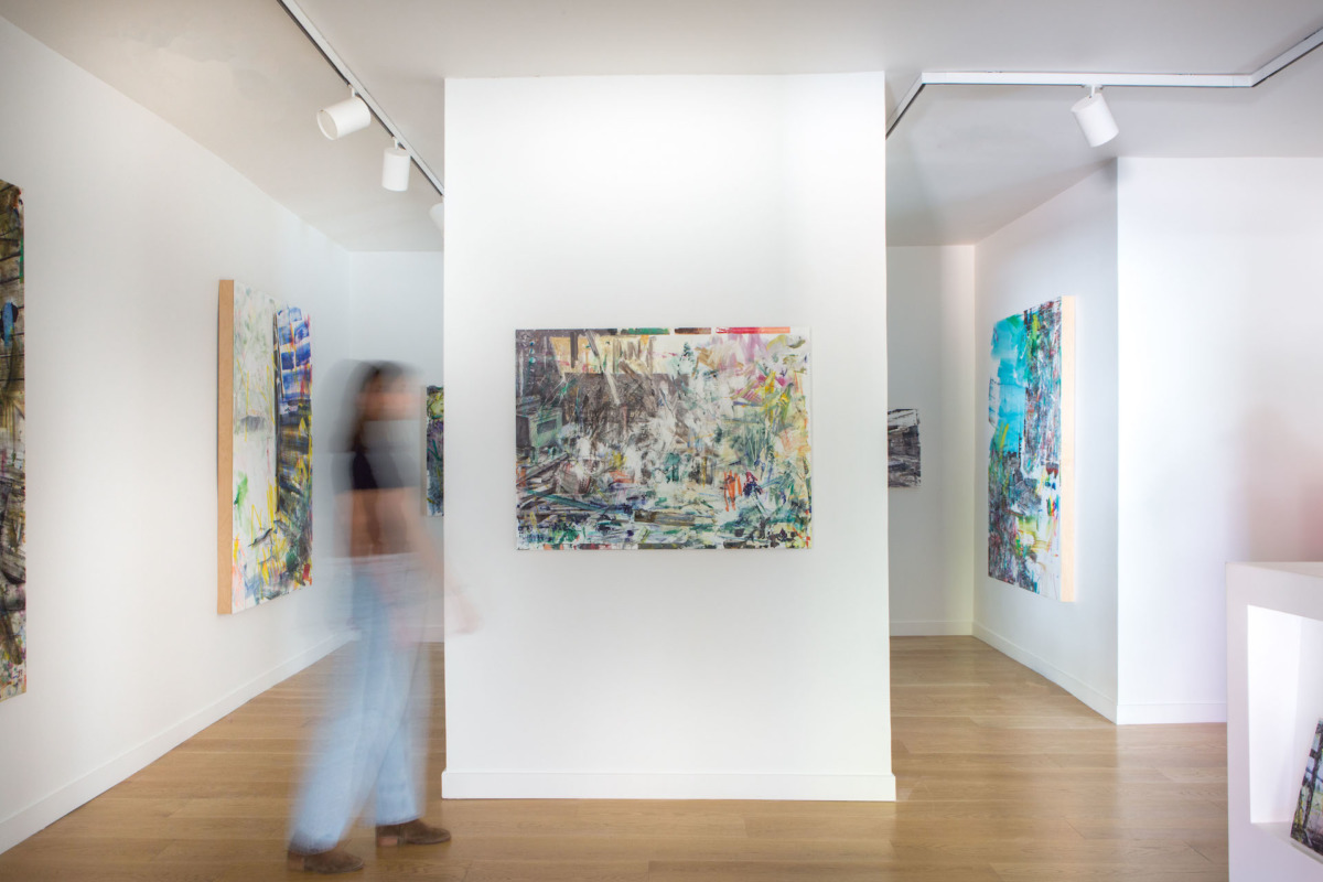 a blurred person walks in front of five modernist colorful paintings on a white wall