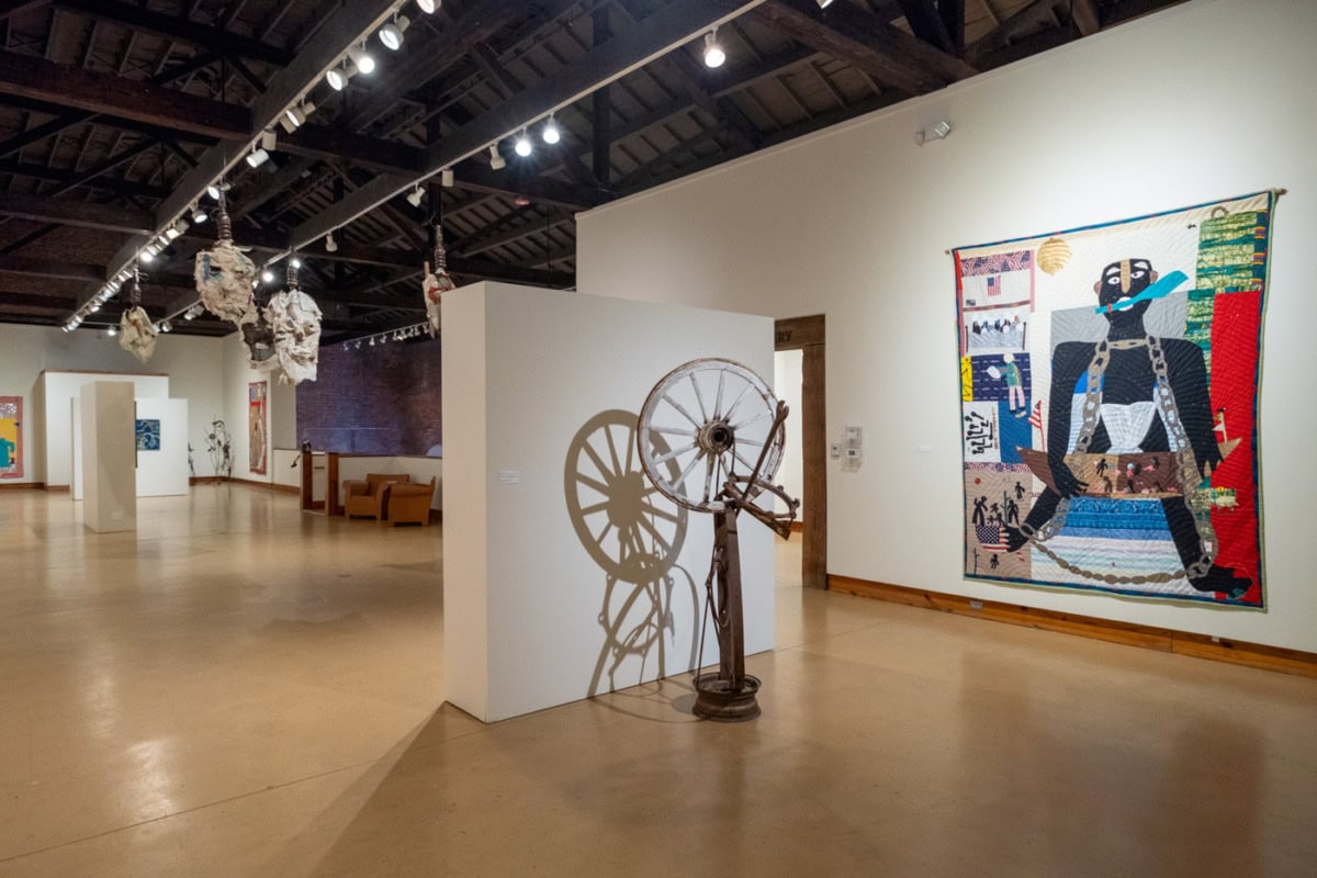 a white gallery space with wooden floors and a sculpture and painting