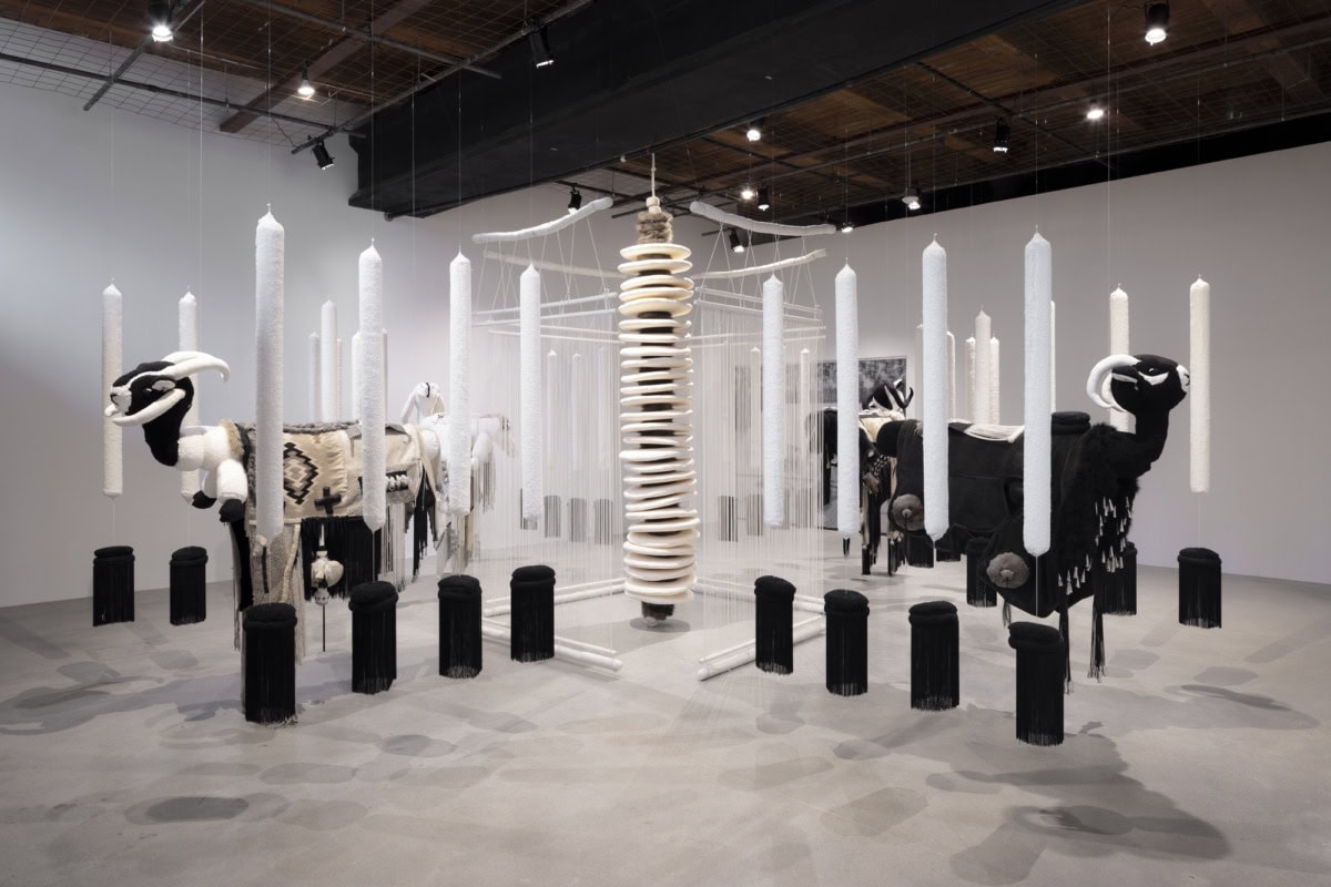 installation view of felt and wool sculptures of sheep hanging from the ceiling