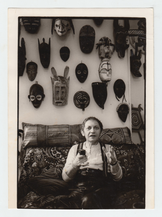 artist sitting in studio wall of masks