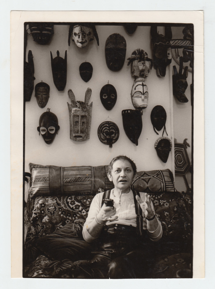 artist sitting in studio in front of wall of African masks