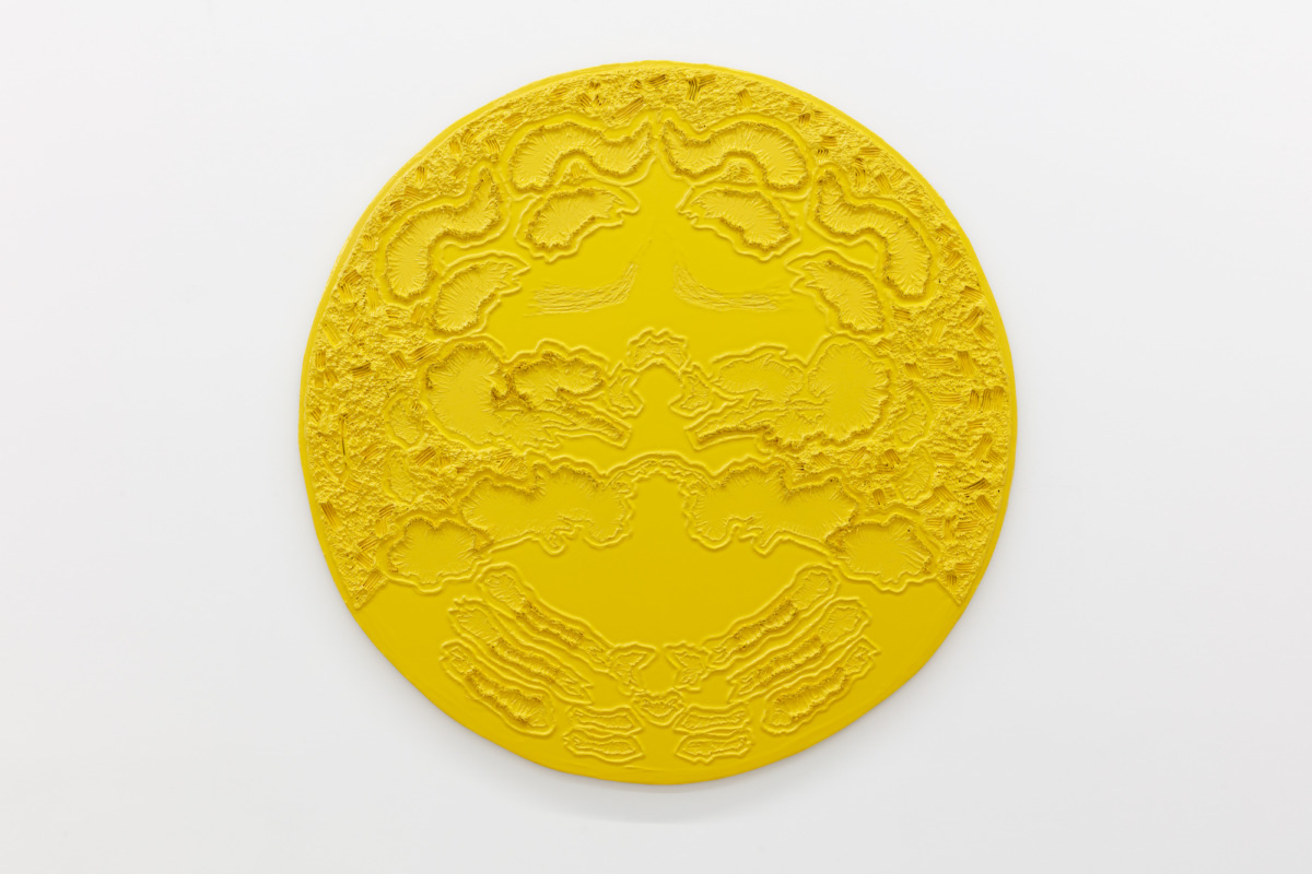 a large circular yellow disk hangs on a white wall with raised details