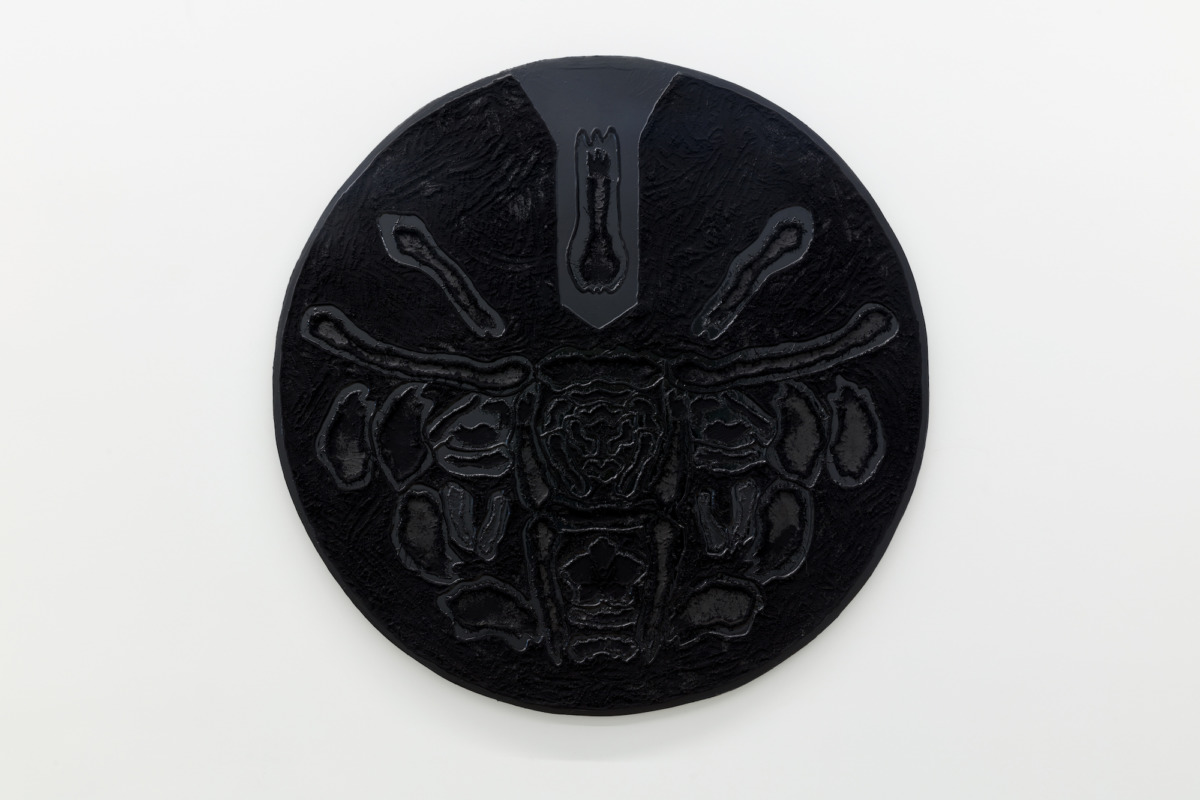 a large black disk hangs on a white wall with an image of a bull in relief