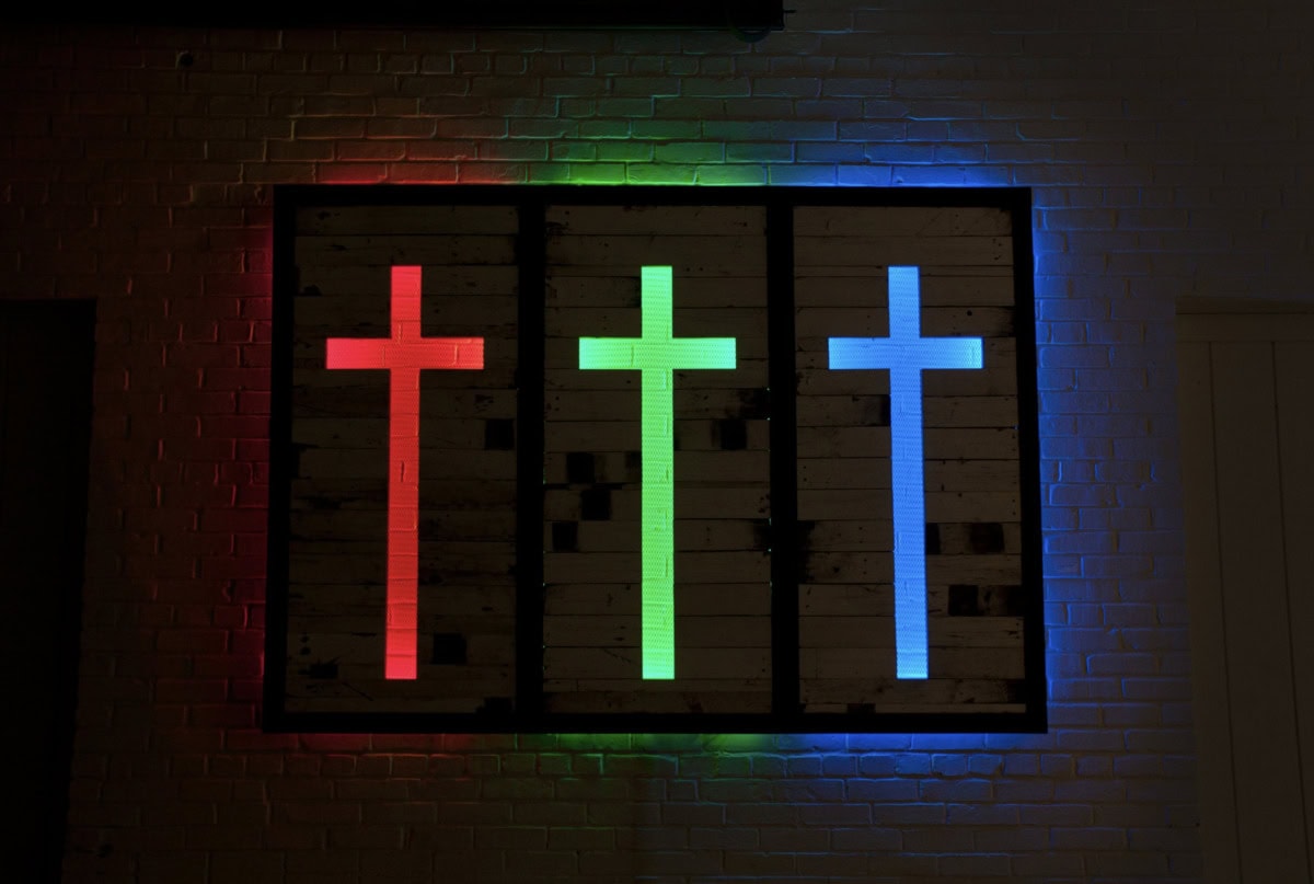 three backlight crucifixes in red, green, and blue light mounted on a wall