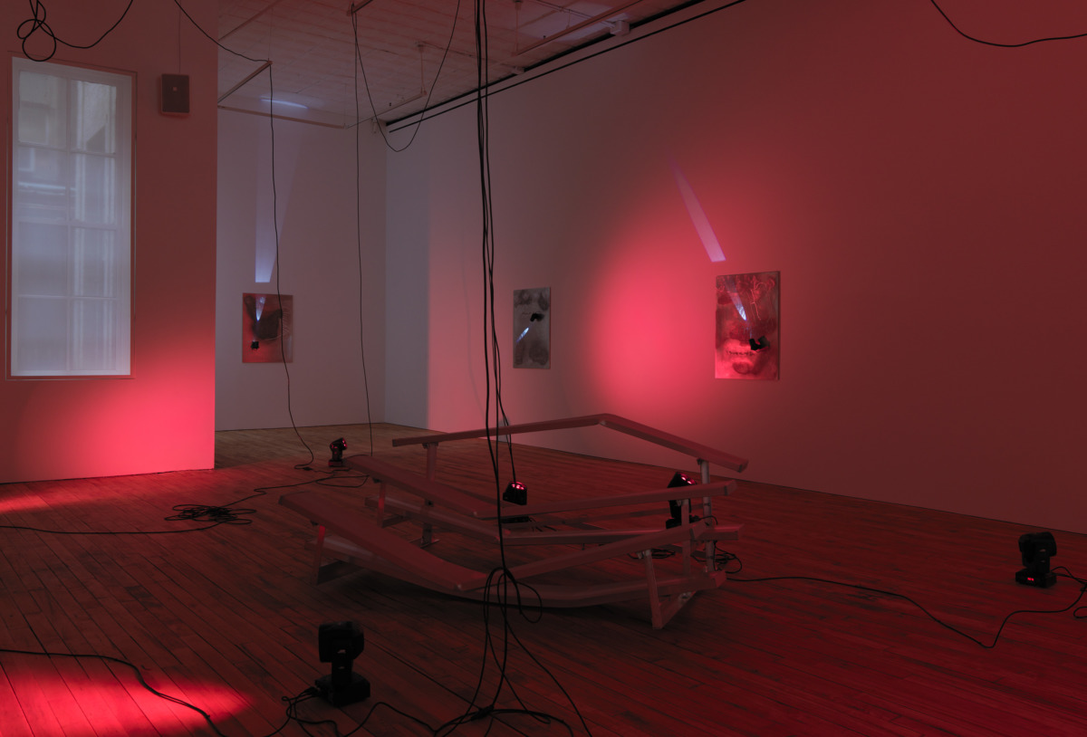 a red lit room with misshapen silver bleachers arranged around the room and with many wires dangling from the ceiling