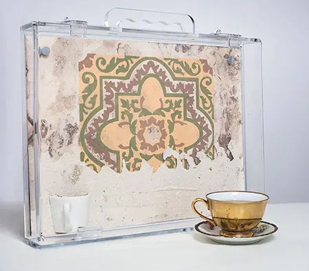 painted tile in glass case next to golden tea cup and saucer small coffee cup embedded in tile yellow green red
