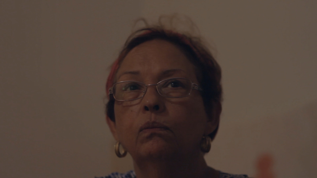 a middle aged woman with short red and black streaked hair and silver rectangle glasses frowns at the camera.