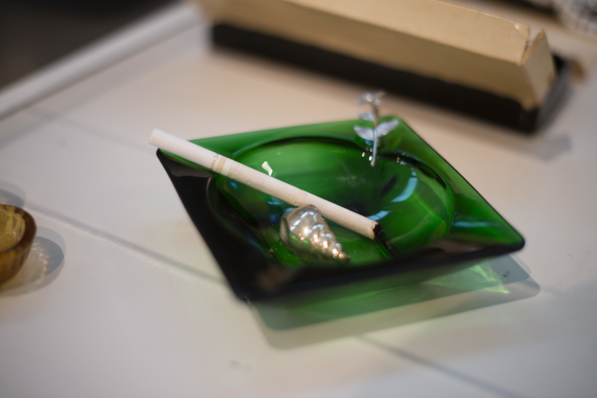 a green glass ashtray holds an unlit Virginia slim cigarette and a silver seashell. 